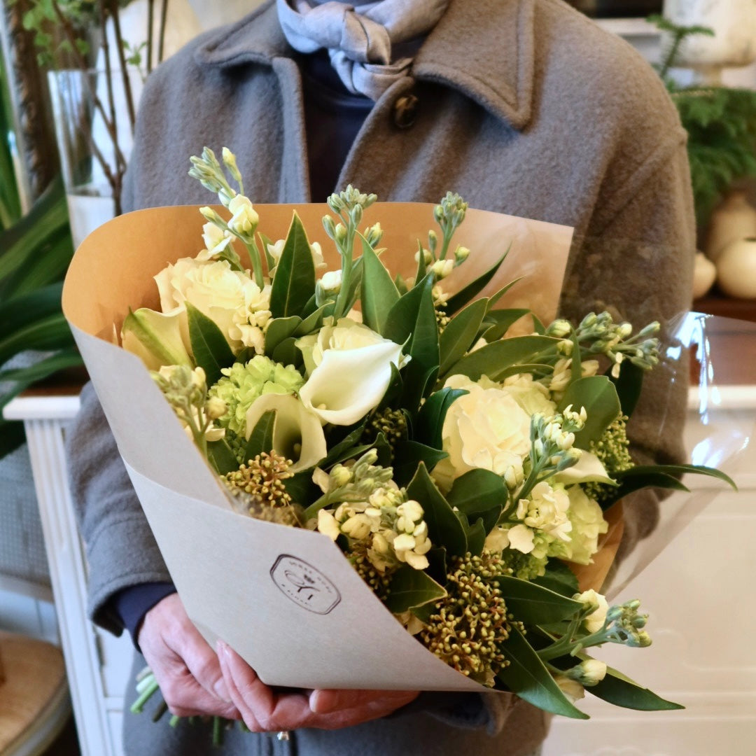 Person holding a bouquet of flowers wrapped in brown paper.