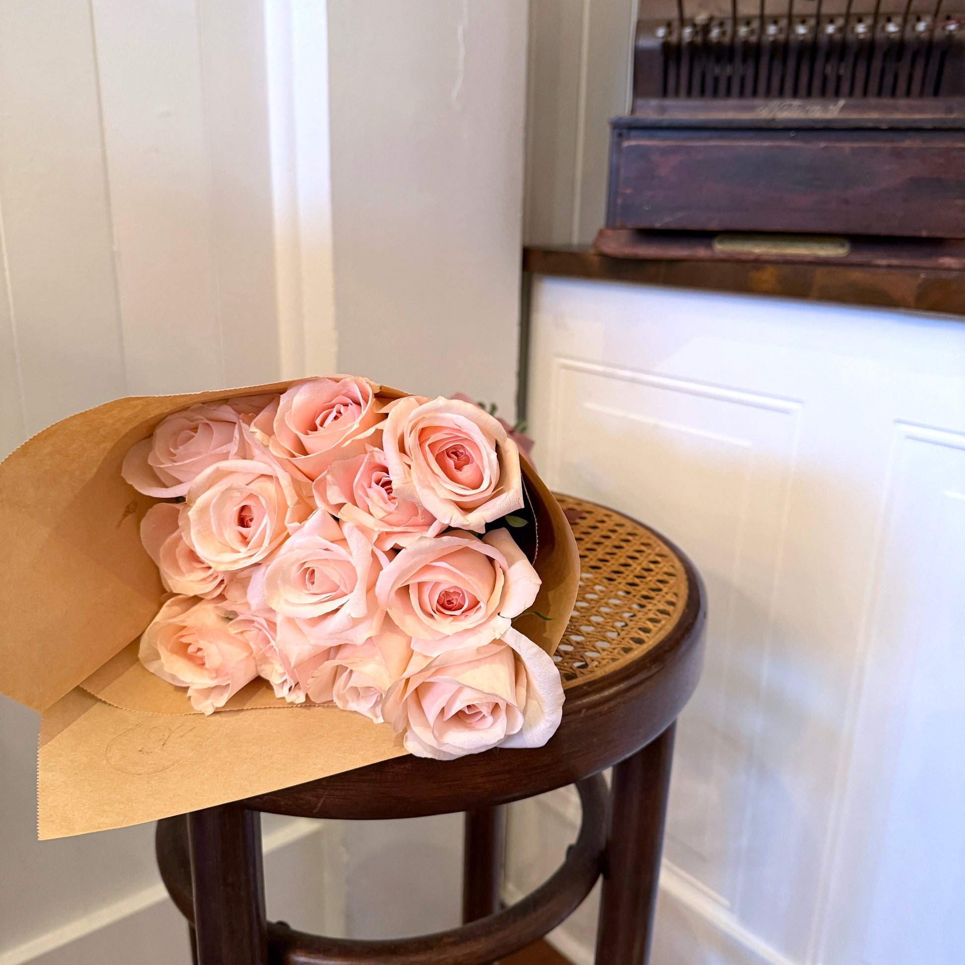 Bouquet of pink roses wrapped in brown paper on a wooden stool against a white wall.