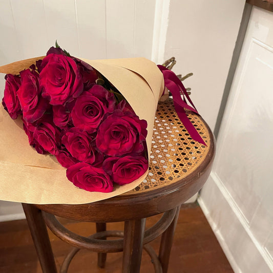Bouquet of red roses on a wooden stool against a white wall.