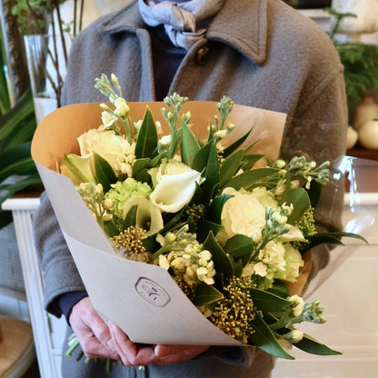 Person holding a bouquet of flowers wrapped in brown paper.
