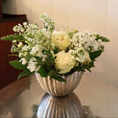 Bouquet of white and green flowers in a textured vase on a reflective surface.